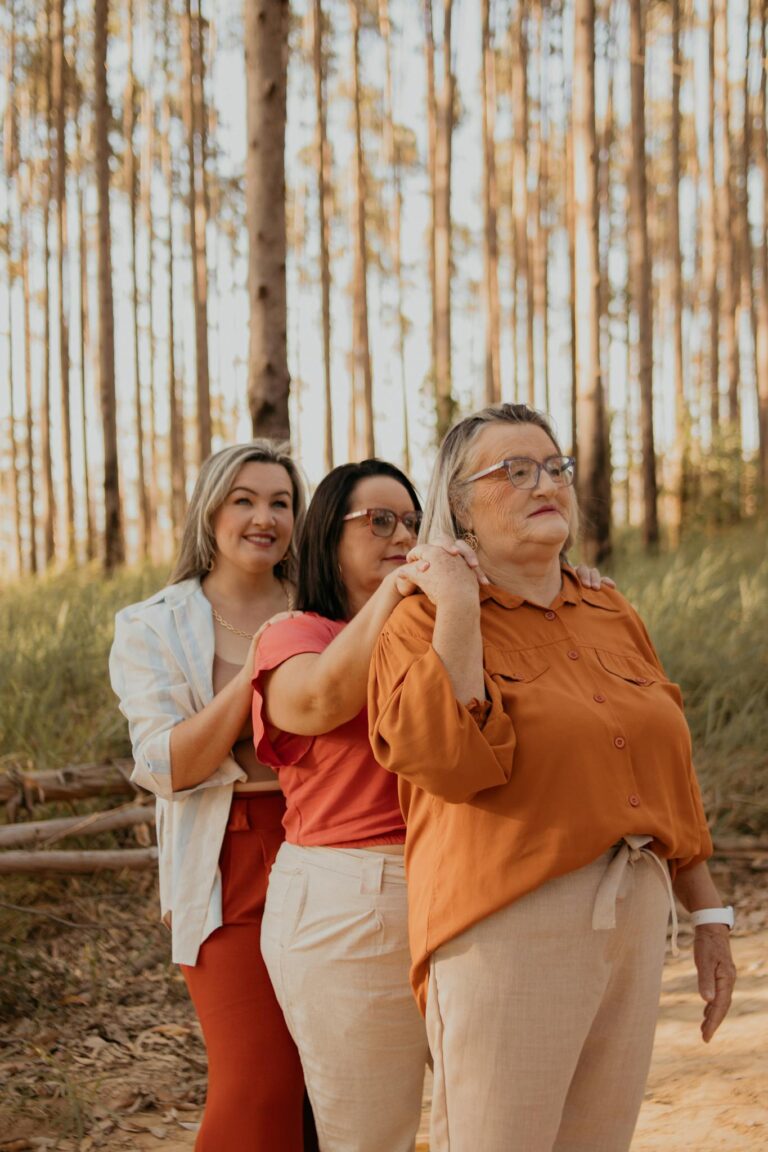 Three women from different generations smiling together outdoors in a forest.