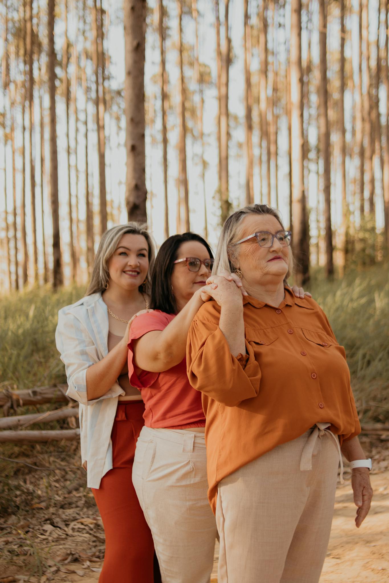 Three women from different generations smiling together outdoors in a forest.