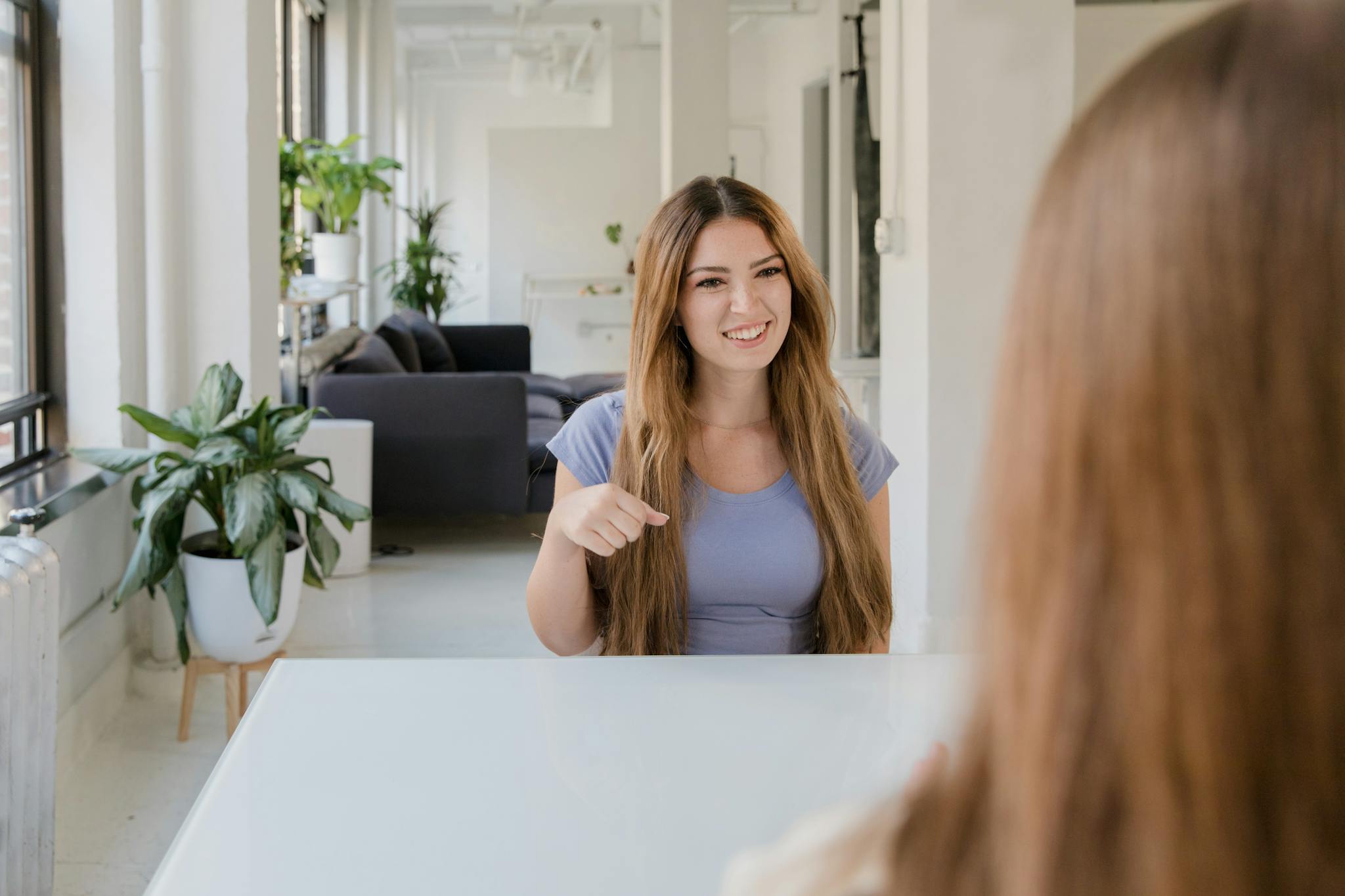 Two women using sign language in a modern indoor setting, promoting deaf community communication.