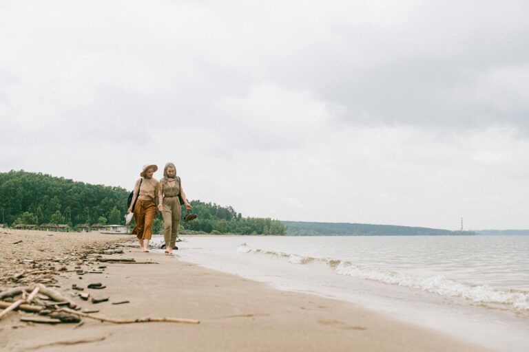 Two women walking together on a calm beach, enjoying the peaceful seaside environment.
