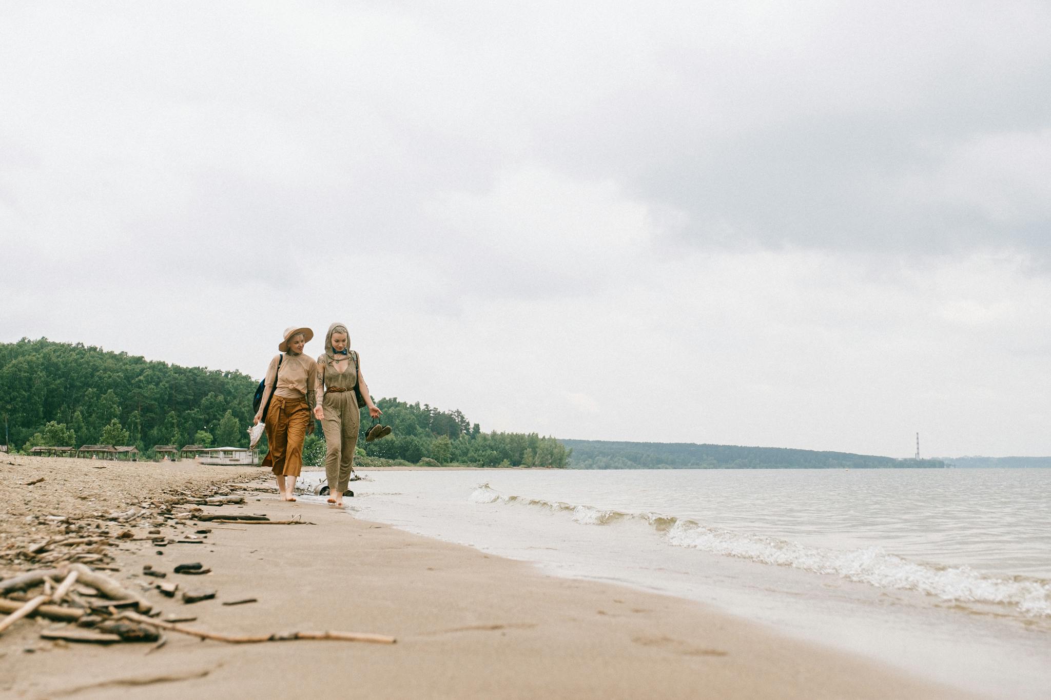 Two women walking together on a calm beach, enjoying the peaceful seaside environment.